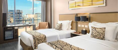 A hotel room with two beds, a desk, a chair, a TV, and a large window with a city view.