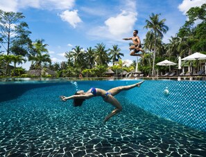 A swimming pool with tiled flooring, surrounded by palm trees and lounge chairs.