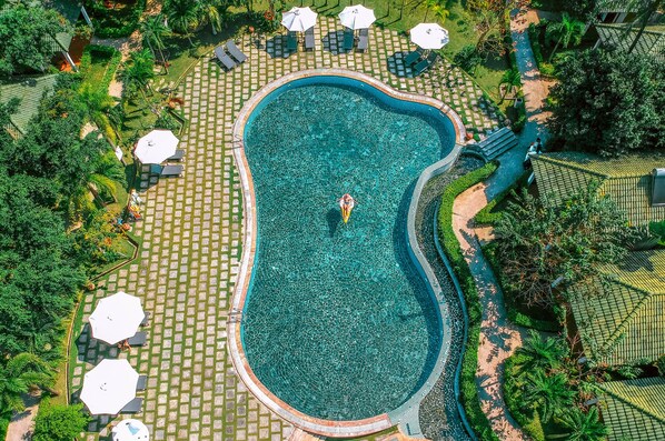 An aerial view of a swimming pool surrounded by lounge chairs and umbrellas, with a person in the water.