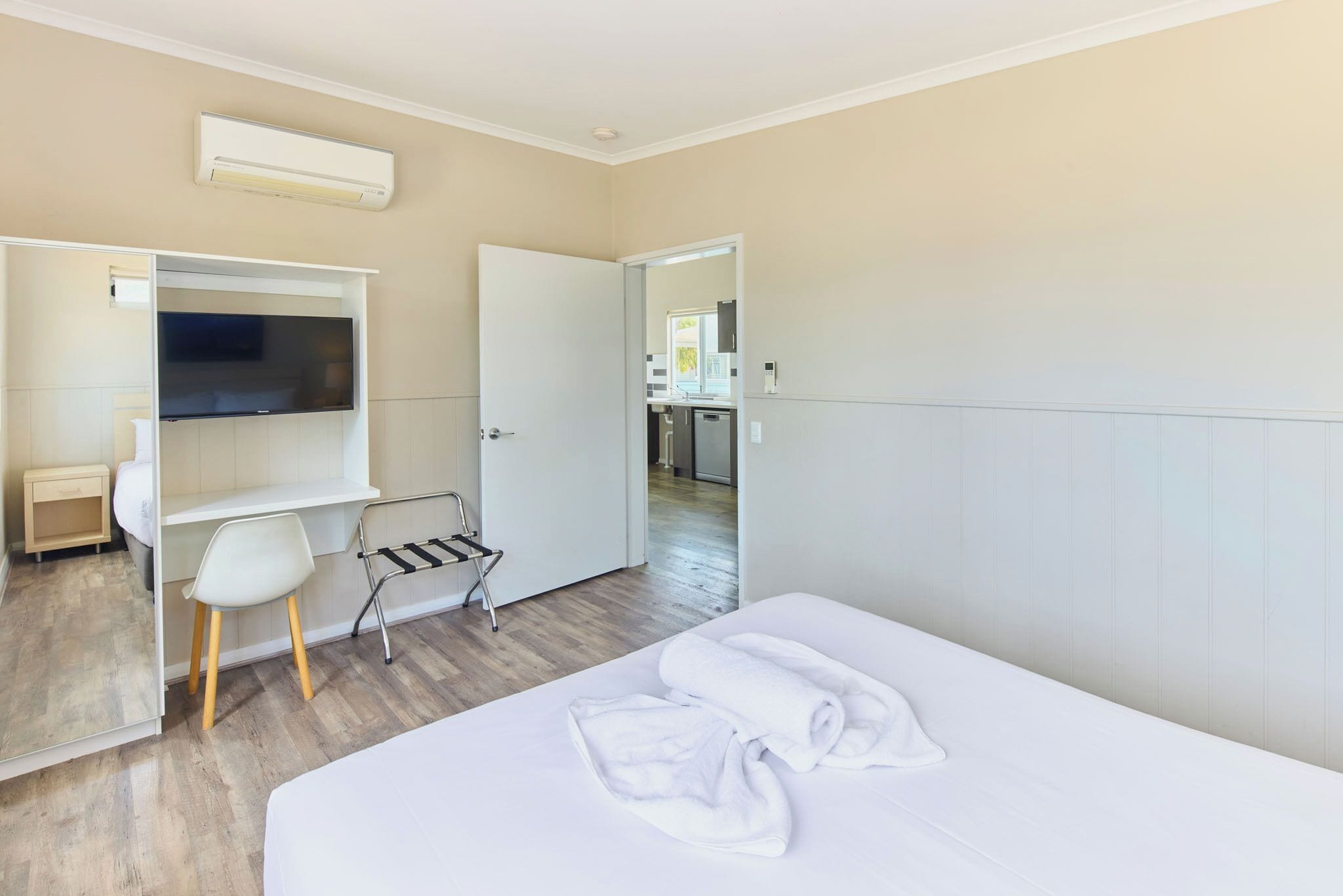 A modern hotel room with a bed, a TV, a desk, and a chair.
