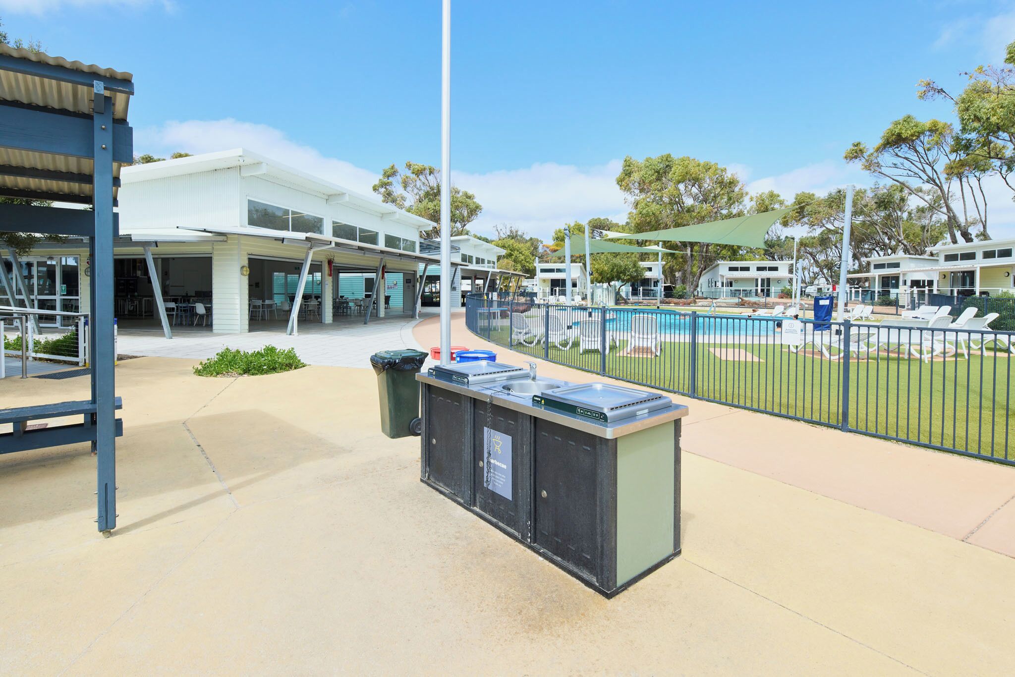 A pool area with a fence, a trash bin, and a water fountain.