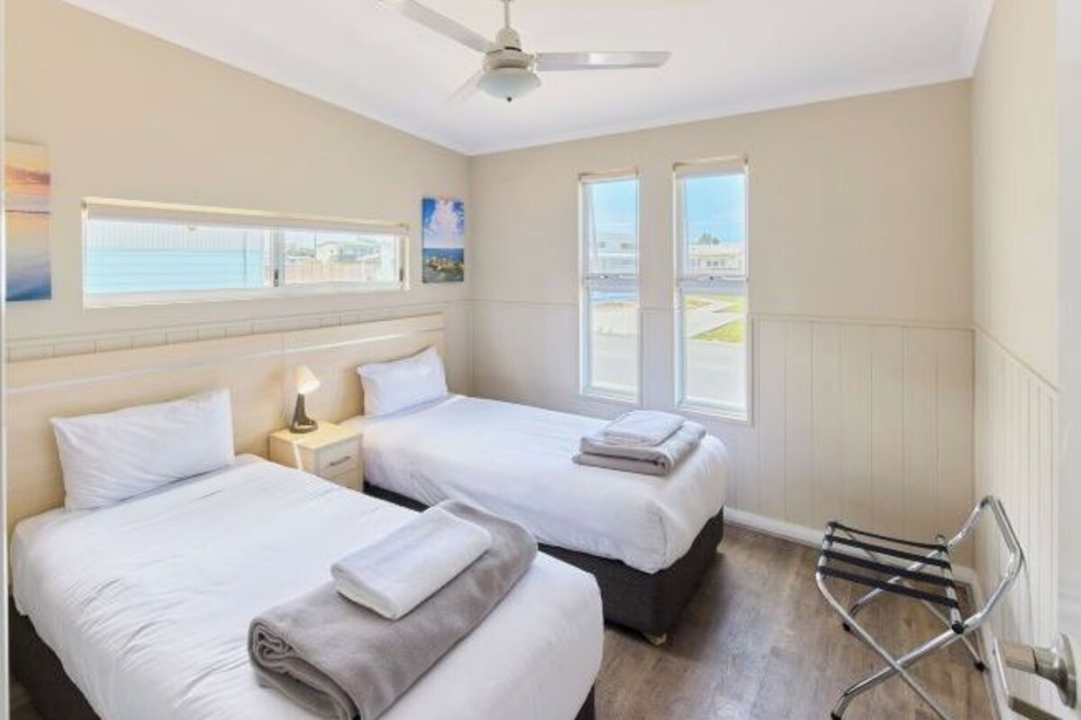 A hotel room with two beds, a ceiling fan, a window with a view, and a towel rack.