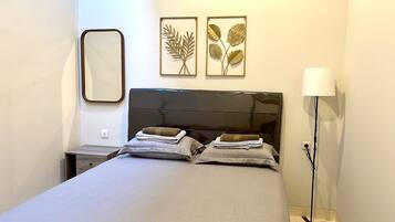 A bedroom with a bed, two pillows, a bedside table, a lamp, and two wall art pieces.