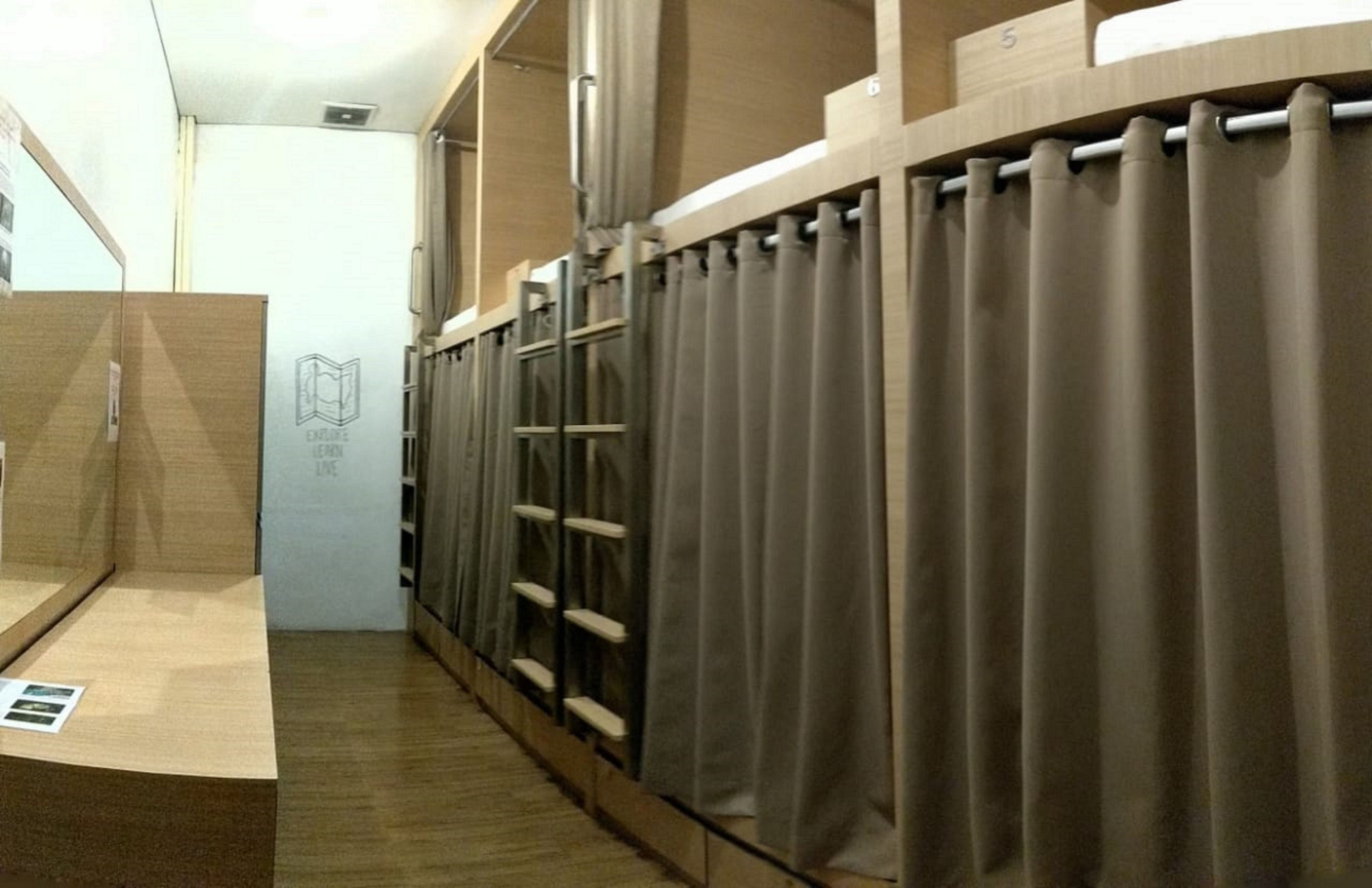Une chambre d’hôtel avec un plancher en bois, un lit avec une tête de lit, une fenêtre avec des rideaux et une petite table avec une chaise.