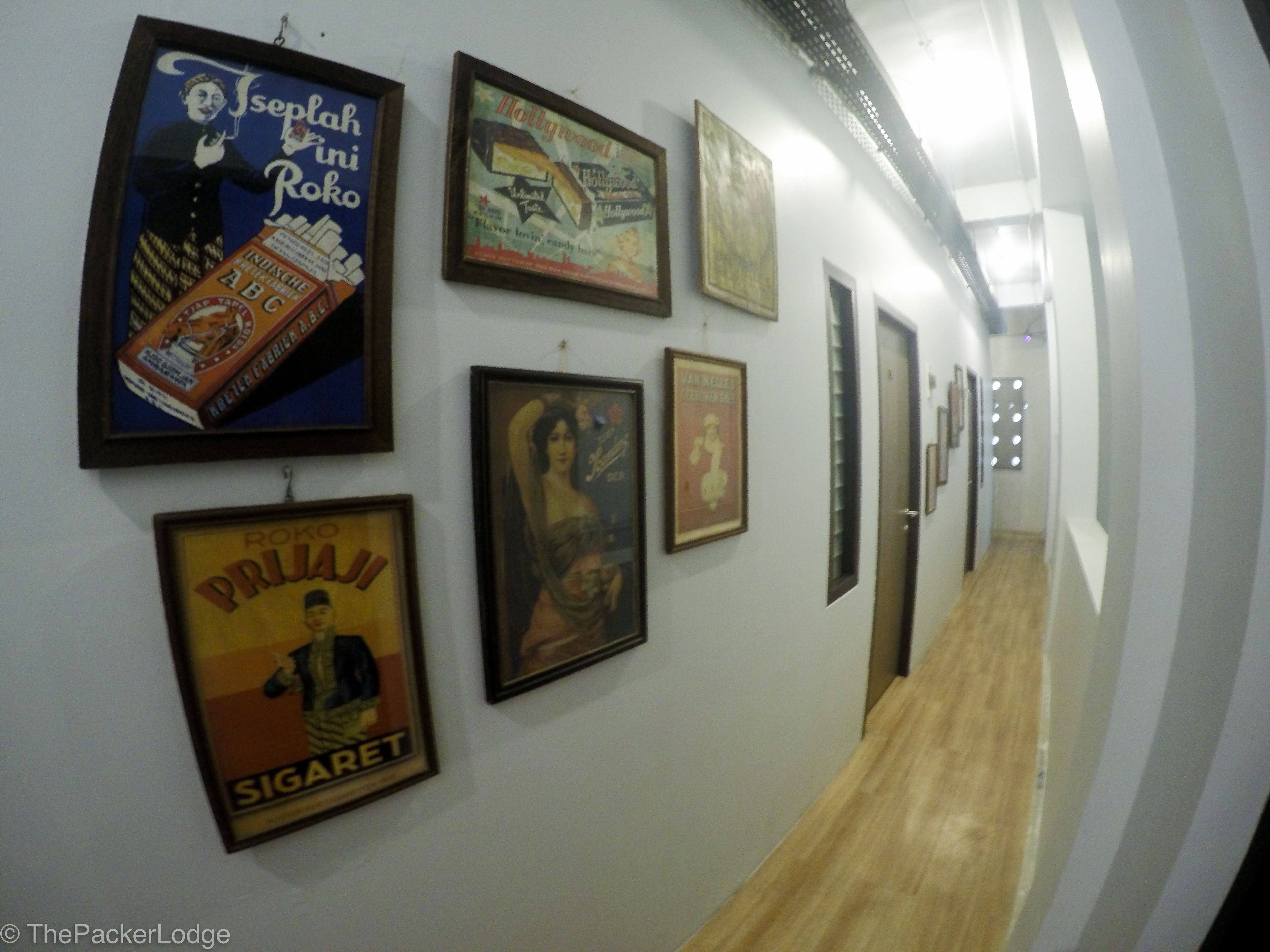 A hallway with framed posters on the walls, a wooden floor, and doors on the right.