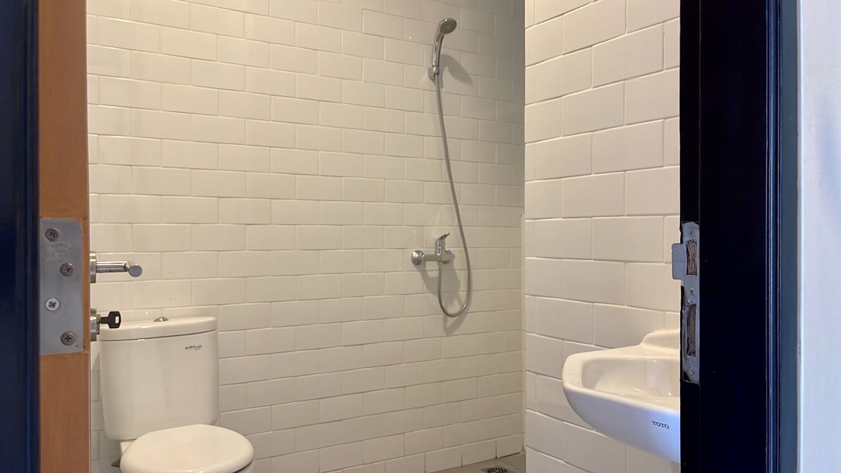 A small, white-tiled bathroom with a toilet, a shower, and a sink.