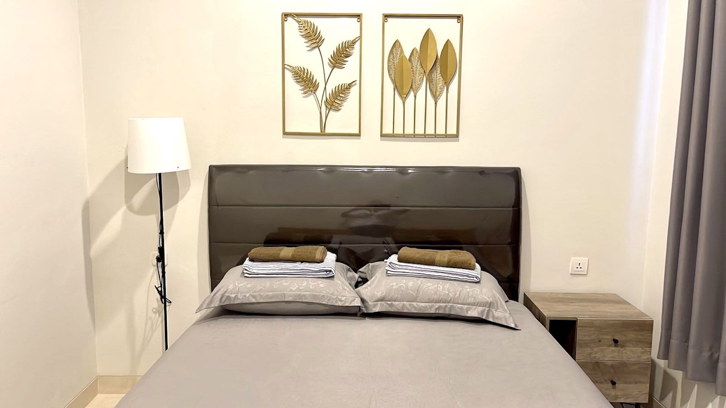 Un lit bien fait, avec deux oreillers, une lampe de chevet et deux œuvres d’art encadrées accrochées au mur.