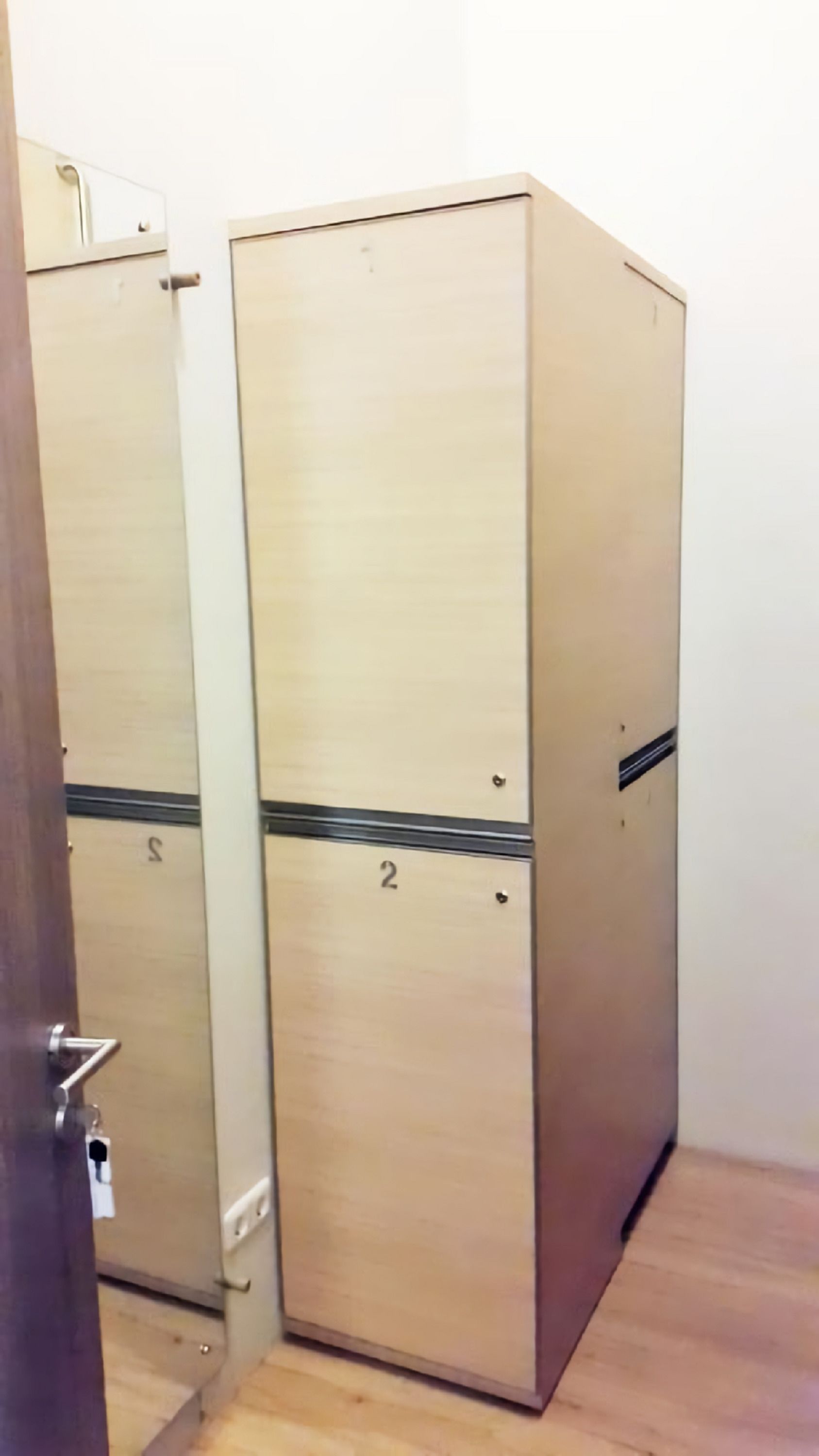 Ένα δωμάτιο με δύο αποδυτήρια σε μπεζ χρώμα, το καθένα με έναν αριθμό που είναι γραμμένος πάνω του.