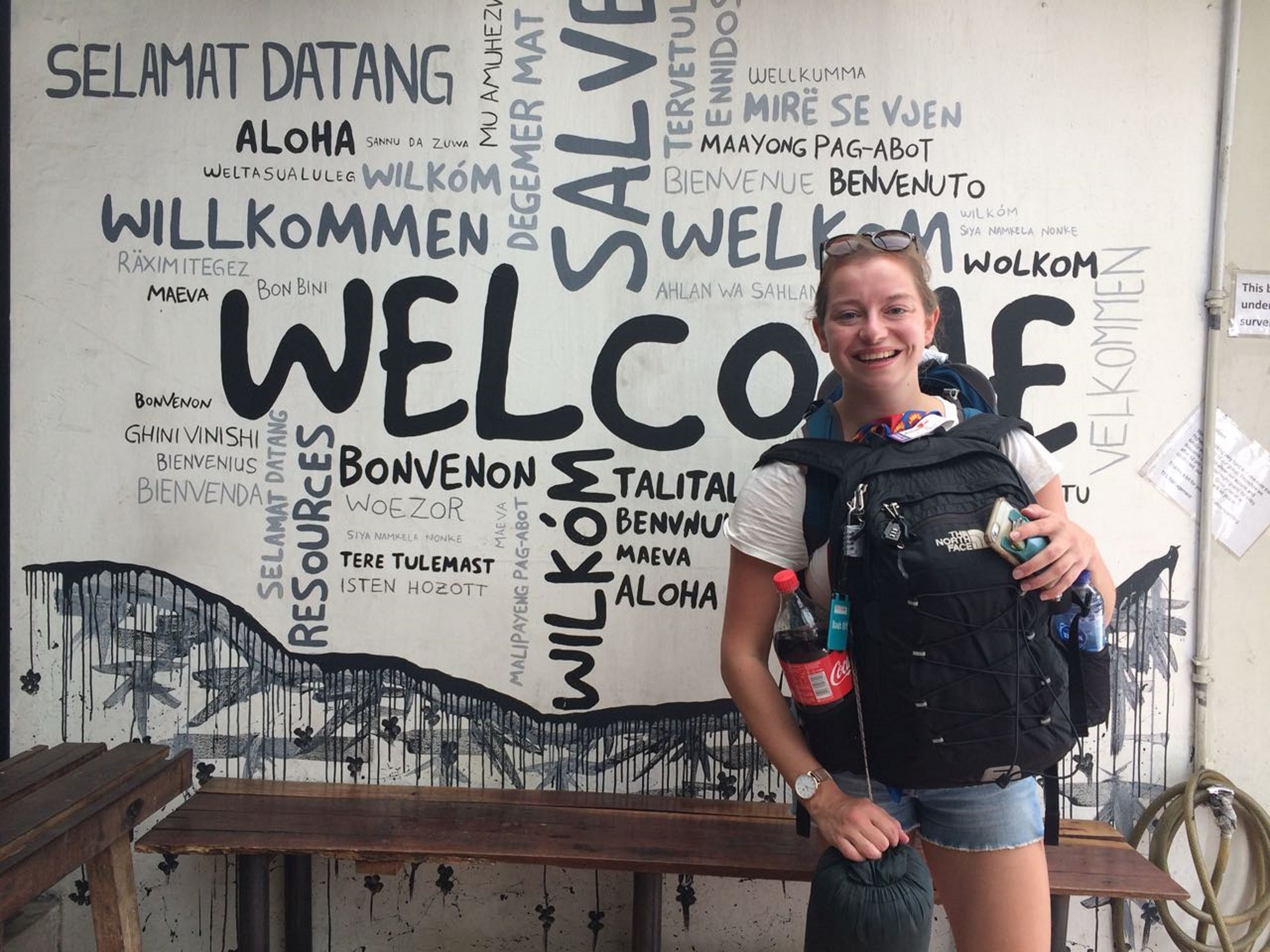 A person standing in front of a wall with various welcome signs in multiple languages.