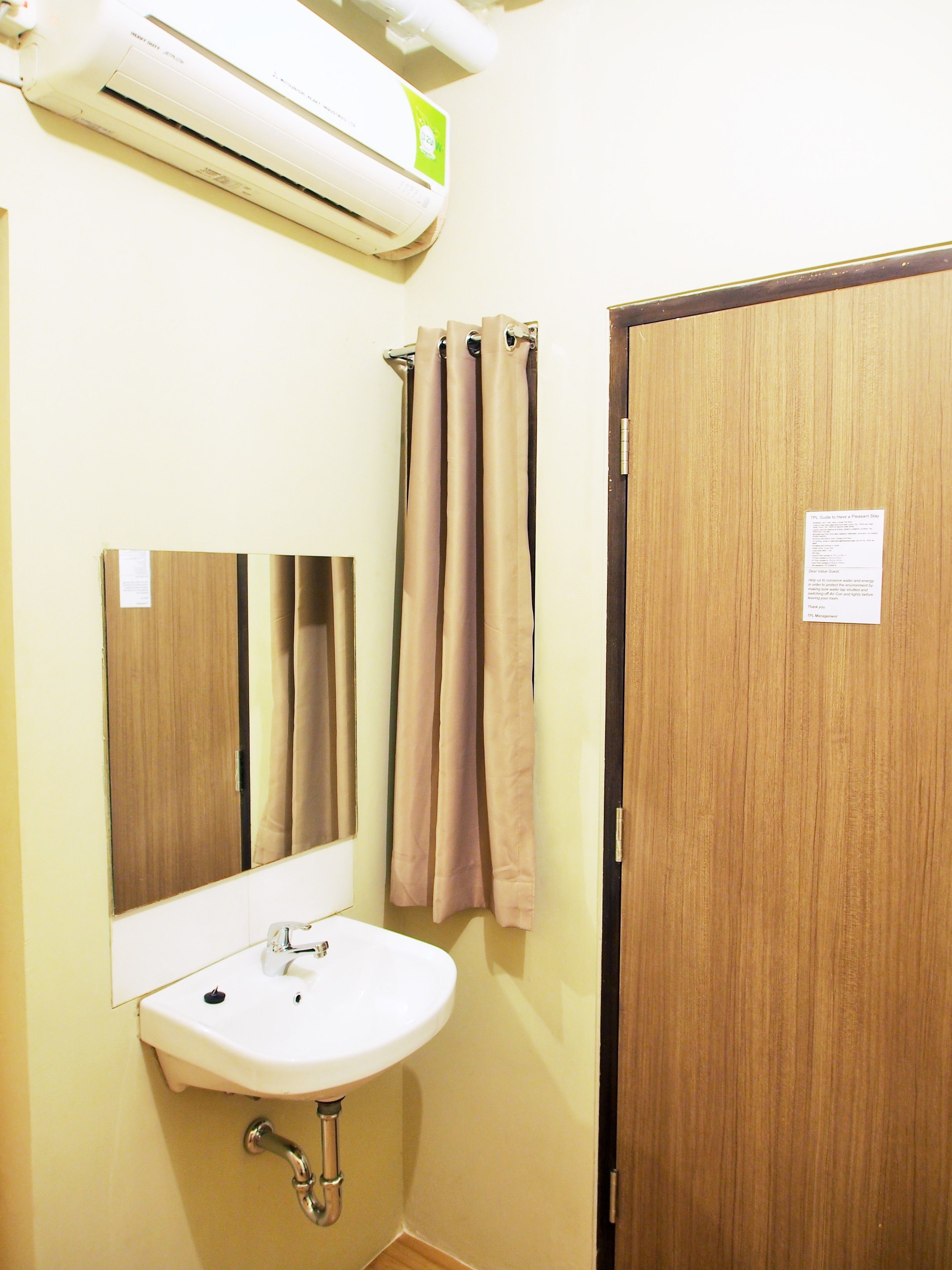 A bathroom with a sink, mirror, shower curtain, and an air conditioning unit.