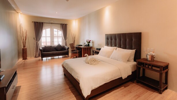 A modern hotel room with a large bed, a sofa, a desk, and a TV. - Kingsley's Hotel and Gastro Pub (Mabalacat City)