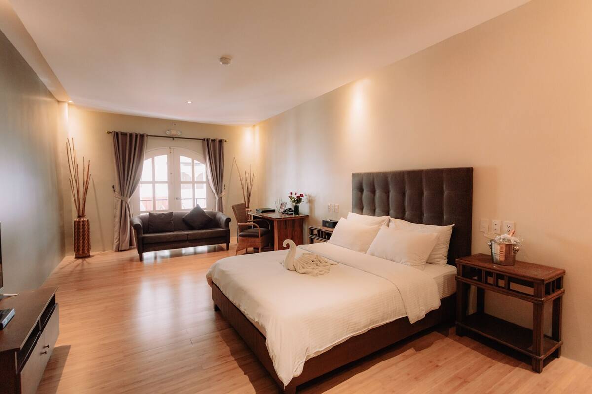 A modern hotel room with a large bed, a sofa, a desk, and a TV.