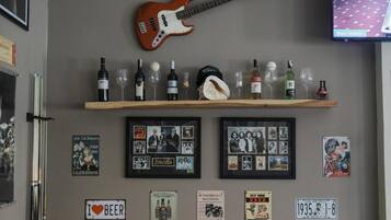 Una pared con una guitarra, un estante con botellas y vasos, y varias fotos y carteles enmarcados.