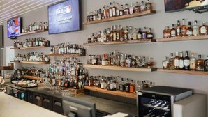 A bar area with shelves of liquor bottles, a television displaying MLB.TV, and a bar counter with glasses and a coffee machine. - Kingsley's Hotel and Gastro Pub (Mabalacat City)