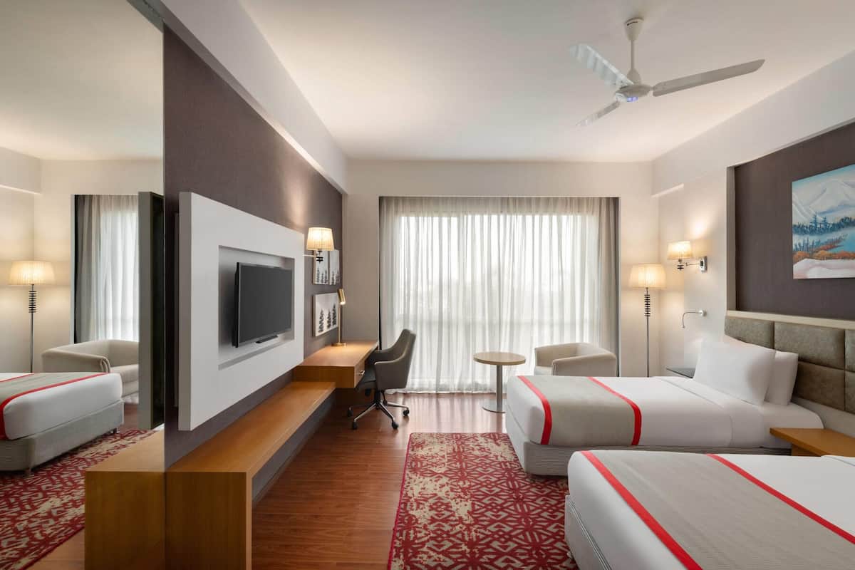 A hotel room with two beds, a TV, a desk, a chair, a small table, and a ceiling fan.