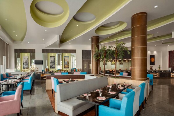 A spacious hotel lobby with multiple seating areas, a central column, and a large screen on the wall.
