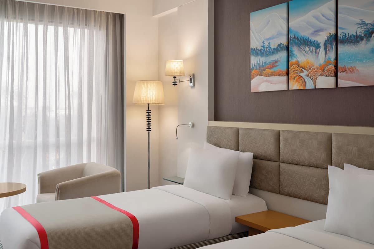 A hotel room with a bed, bedside tables, a lamp, a chair, and a painting on the wall.