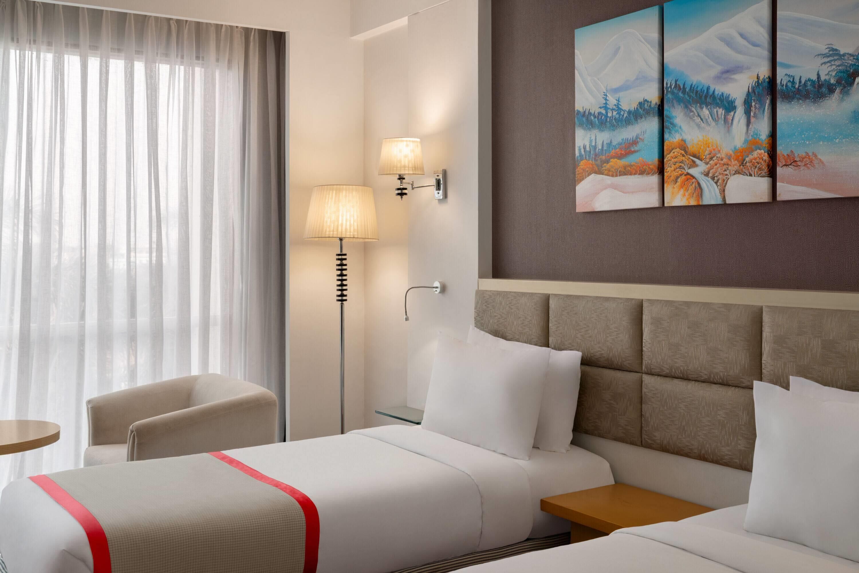A hotel room with a bed, bedside tables, a chair, a lamp, and a painting on the wall.