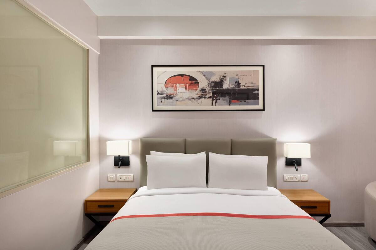 A hotel room with a bed, bedside lamps, a wall-mounted artwork, and a nightstand.