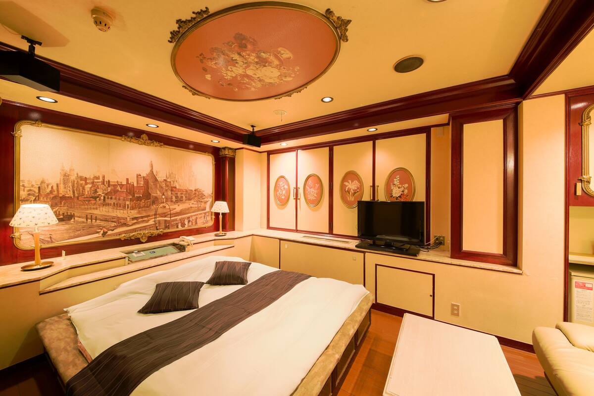 A hotel room with a large bed, a television, a desk, and a wall with a cityscape mural.