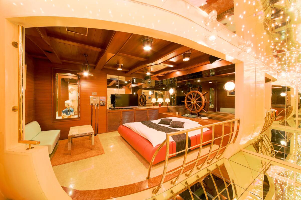 A hotel room with a bed, a small table, a sofa, a TV, and a large mirror.