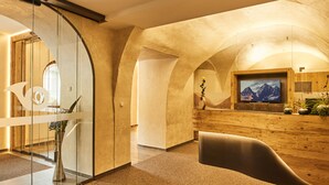 A modern interior with a curved ceiling, a reception desk, and a mounted television. - Hotel Post (Prutz)