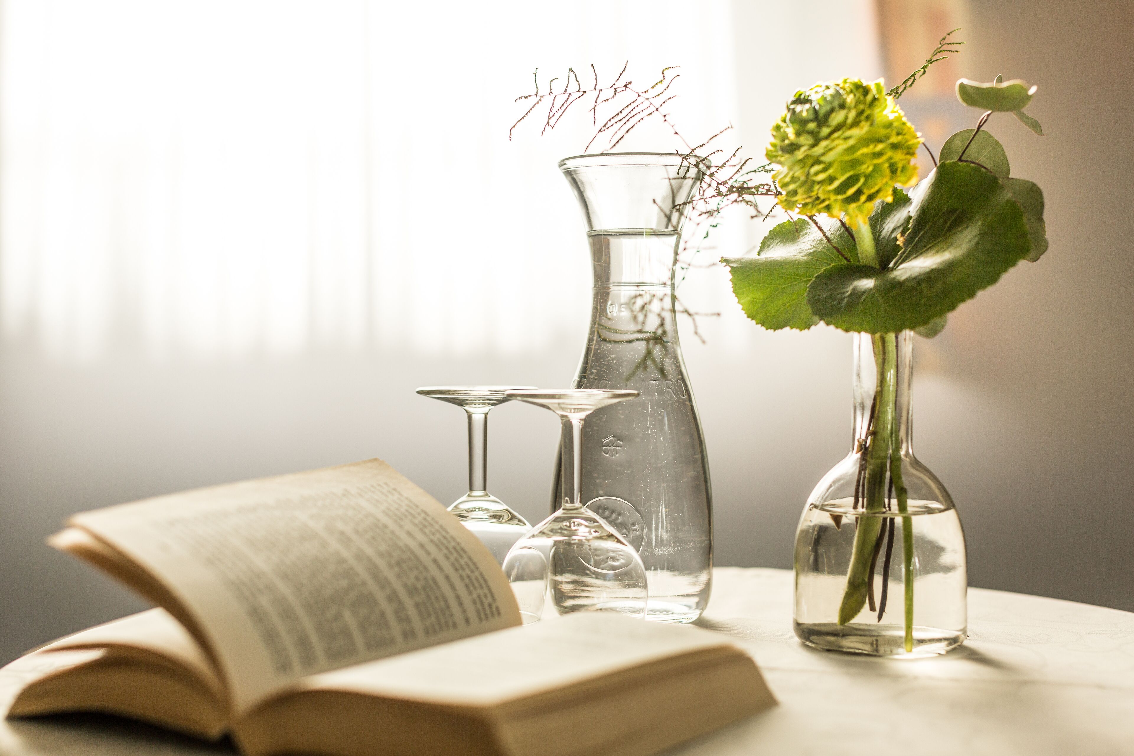 Ein Tisch mit einem Buch, einer Vase mit einer Blume und klaren Glasflaschen.