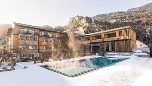 A modern hotel with a pool surrounded by snow, wooden balconies, and a mountainous backdrop. - Hotel Post (Prutz)