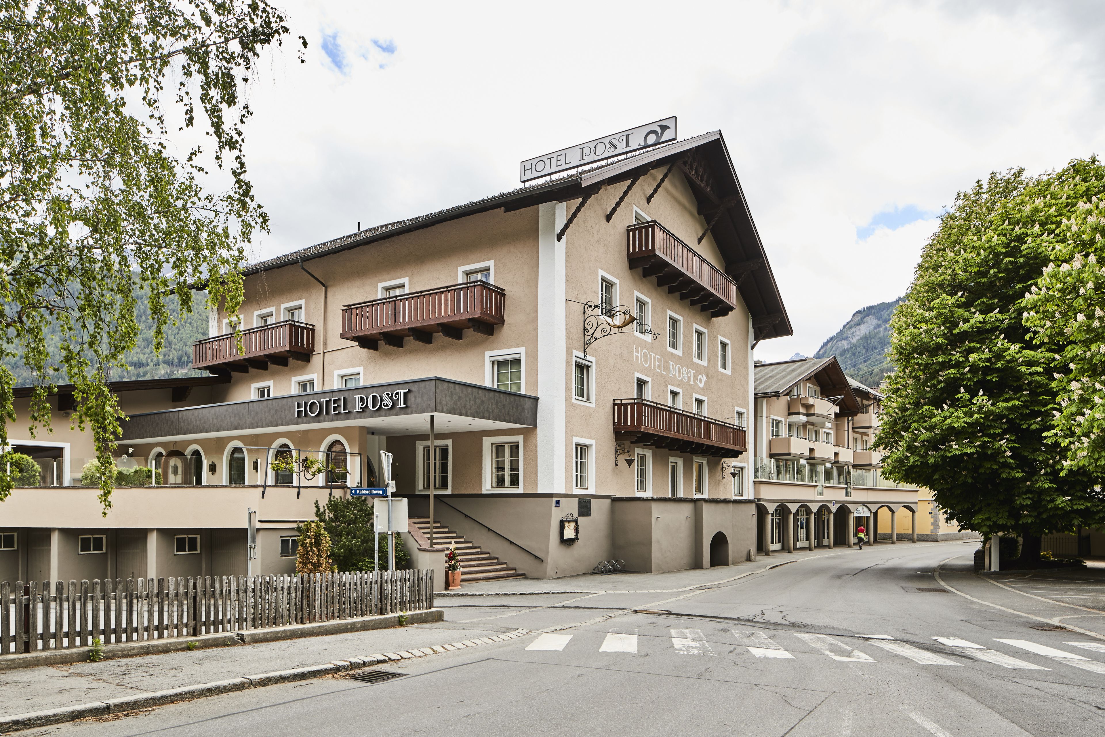 Un hotel de varios pisos con balcones, un letrero que dice "HOTEL POST" y una escalera que conduce a la entrada.