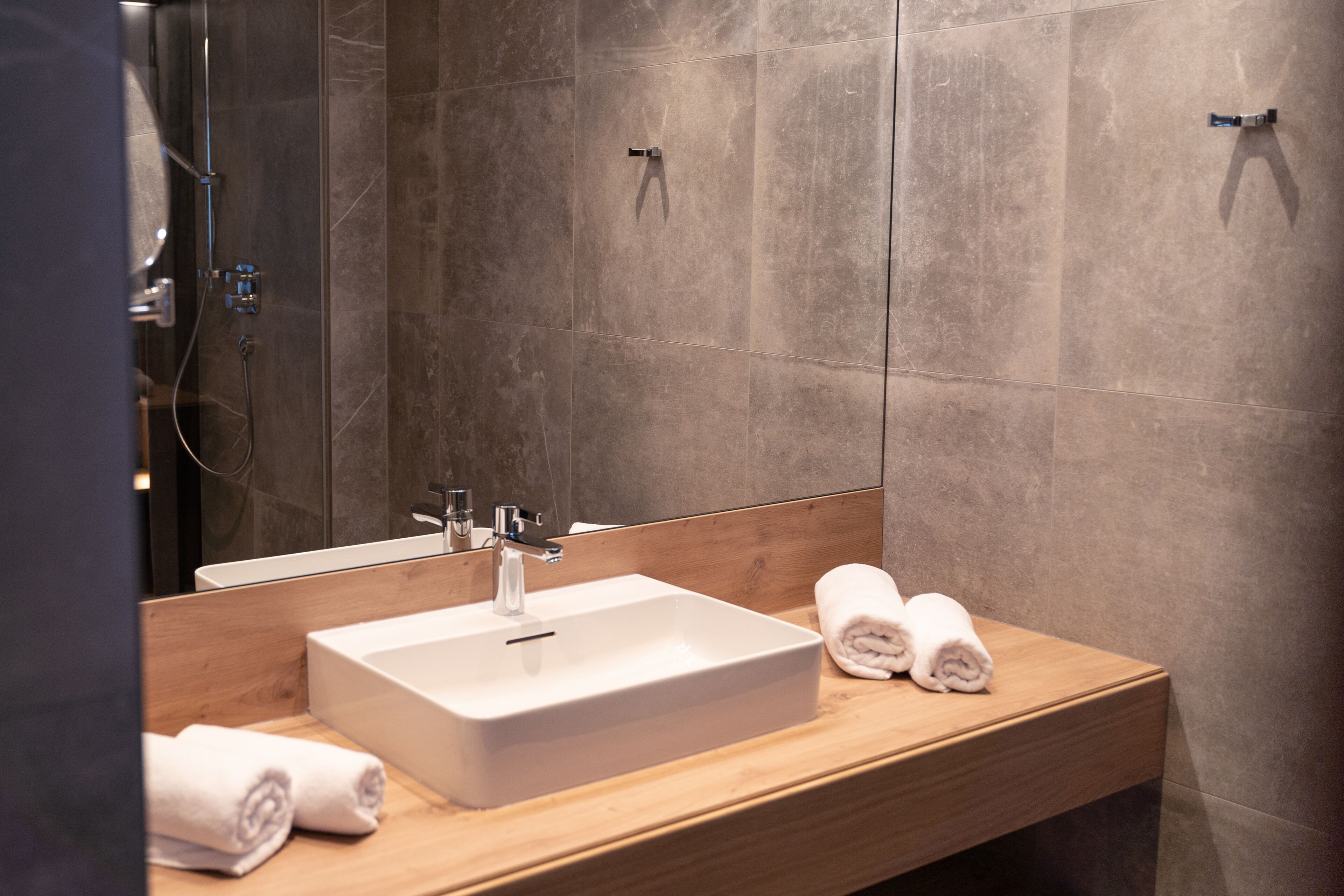 A modern bathroom with a large mirror, a rectangular sink, and two towels on the counter.