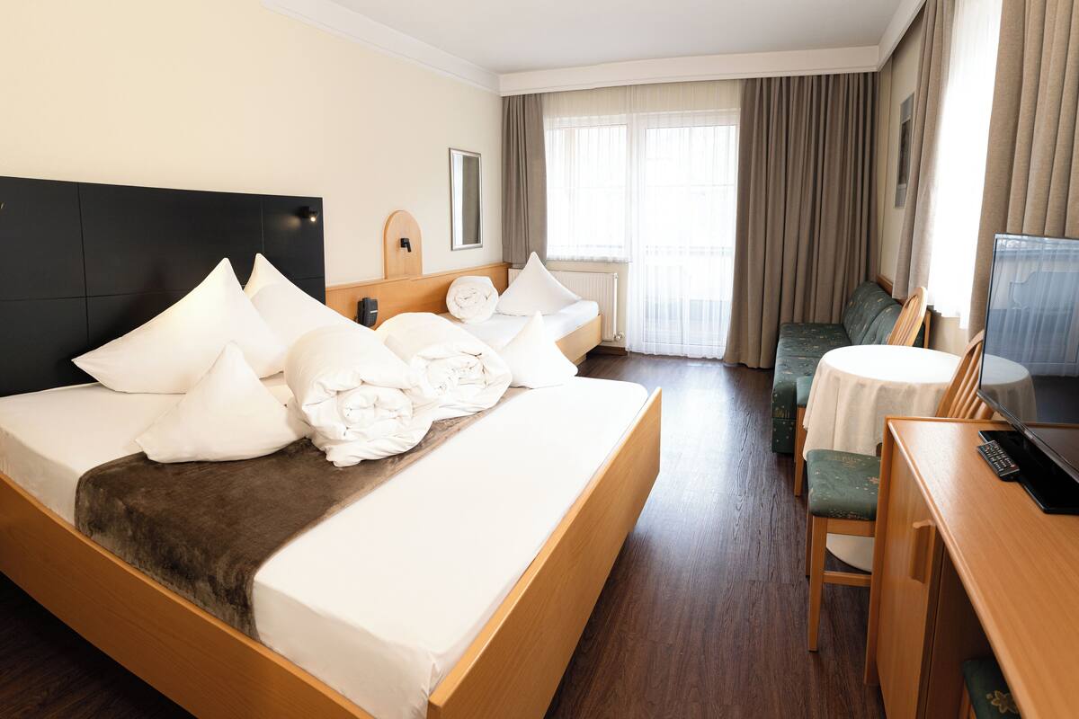 A hotel room with a large bed, a bedside table, a chair, a small round table, and a television.