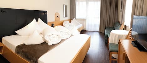 Habitación de hotel con una cama grande, una mesita de noche, una silla, una pequeña mesa redonda y un televisor.