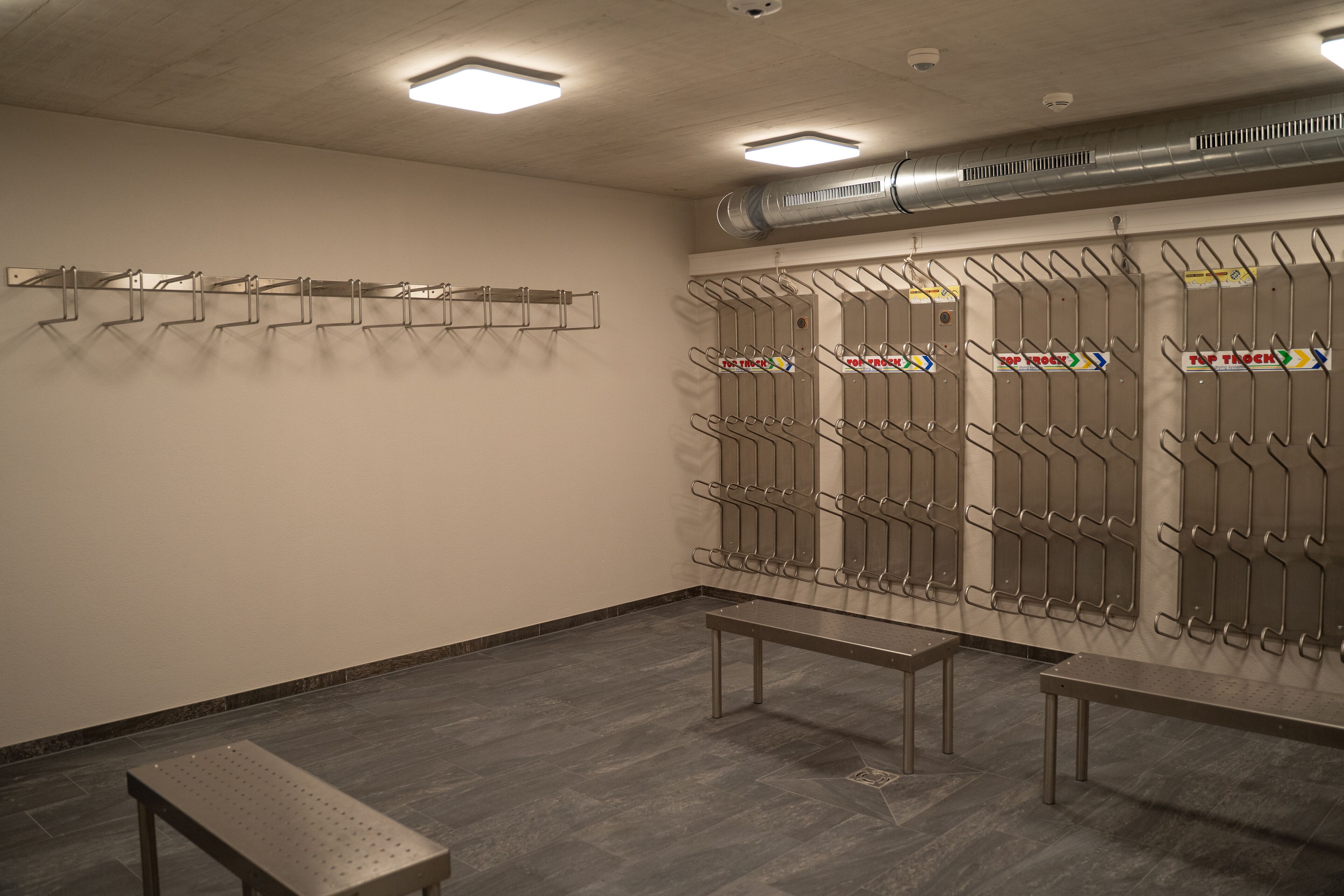A restroom with metal benches, a wall-mounted towel rack, and a ventilation system.