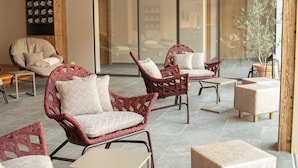 A spacious indoor area with wicker furniture, a large window, and a wooden ceiling. - Hotel Post (Prutz)