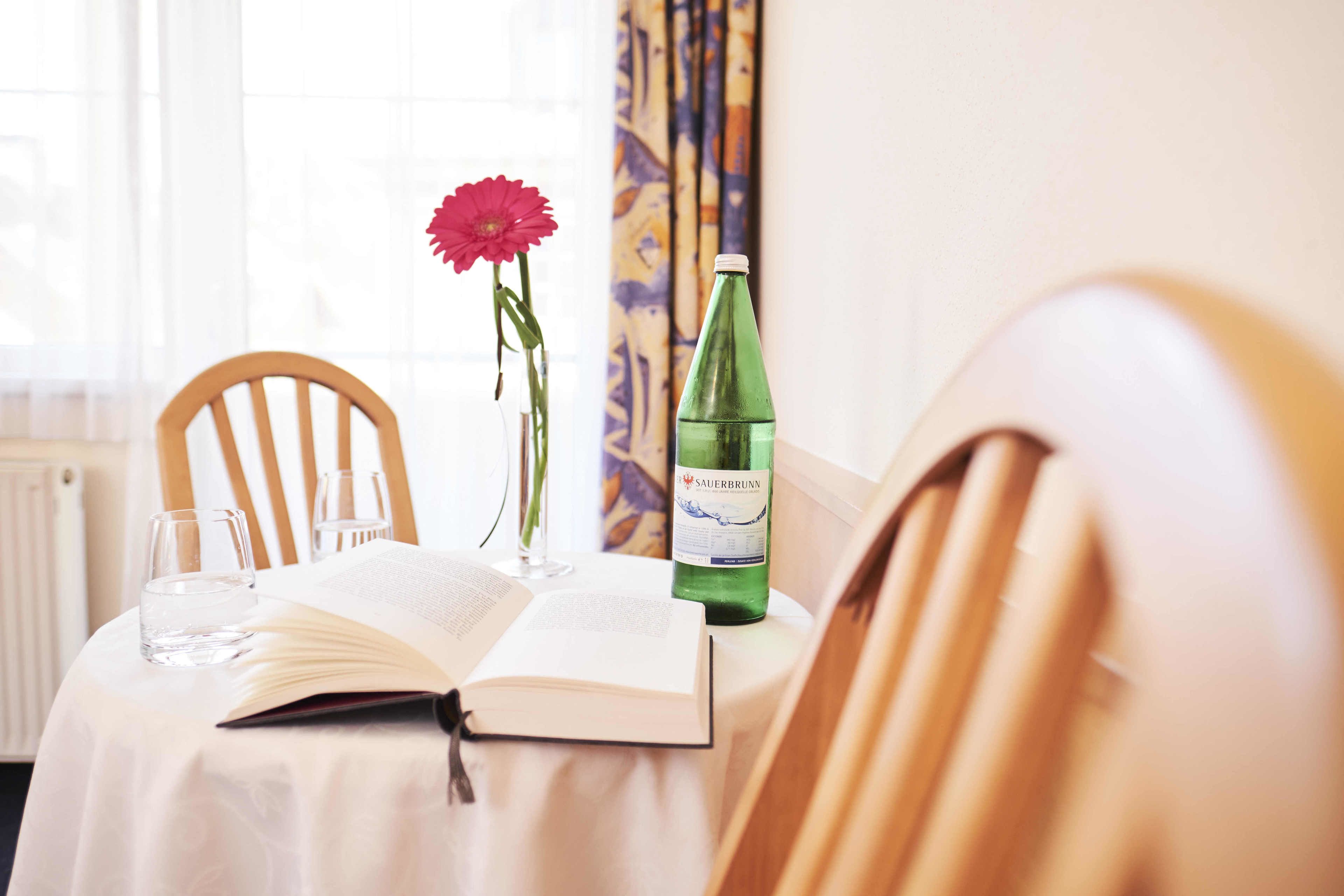 Un tavolo con un libro aperto, un bicchiere d'acqua, una bottiglia di vino e un vaso con un fiore.