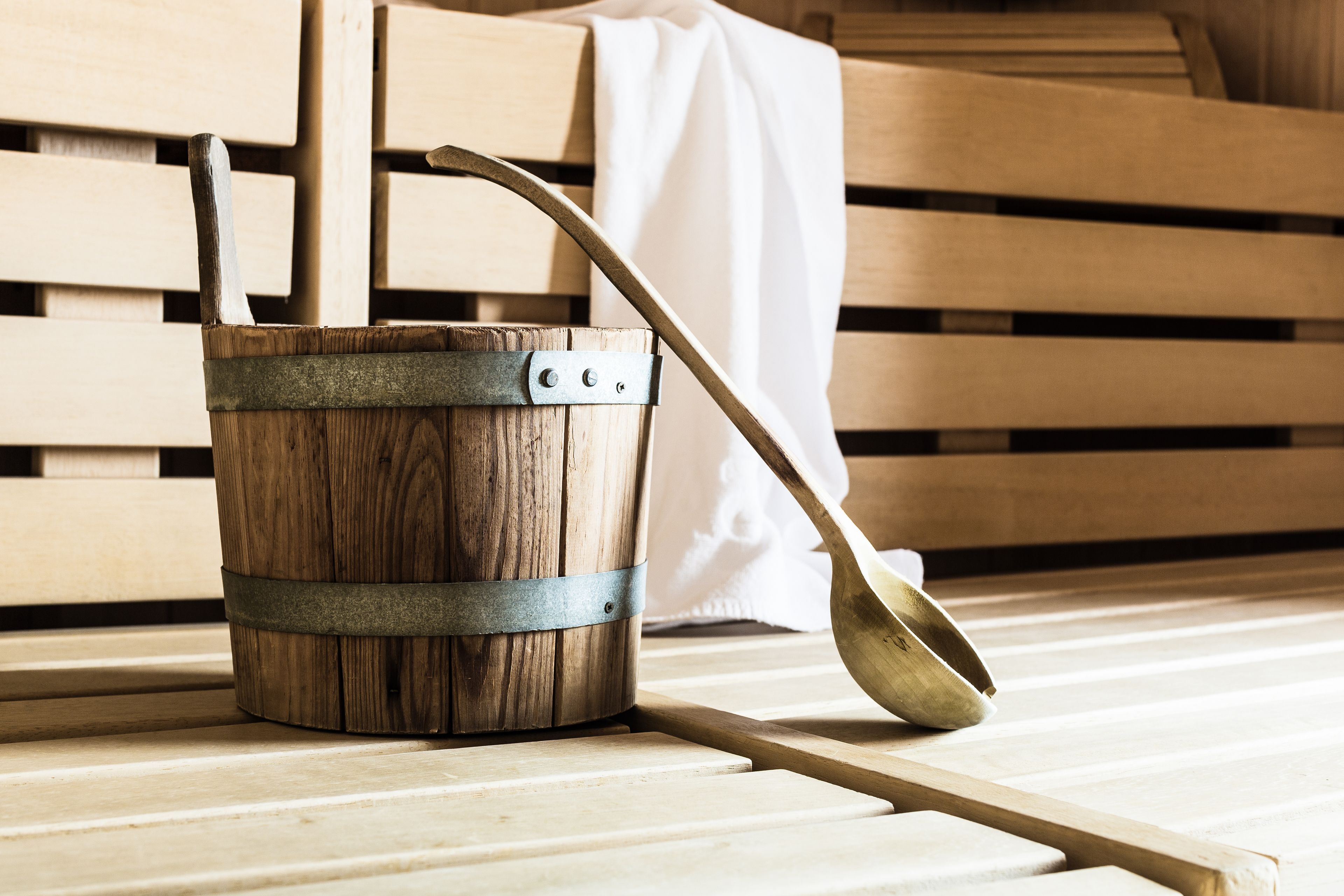 A wooden bucket with a metal strap and a spoon resting on a wooden surface.