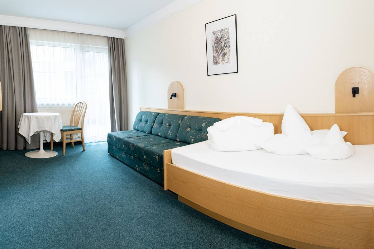 A hotel room with a curved bed, a green sofa, a small table, and a chair.