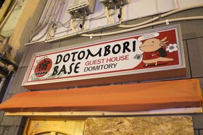 A sign for Dotombori Guest House in a dormitory, with a cartoon character and a red and white color scheme. - Dotombori Base - Hostel (Osaka)