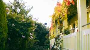 A narrow street with buildings on either side, featuring balconies with flowering plants and a white fence. - Kalithea Apartments (Apokoronas)