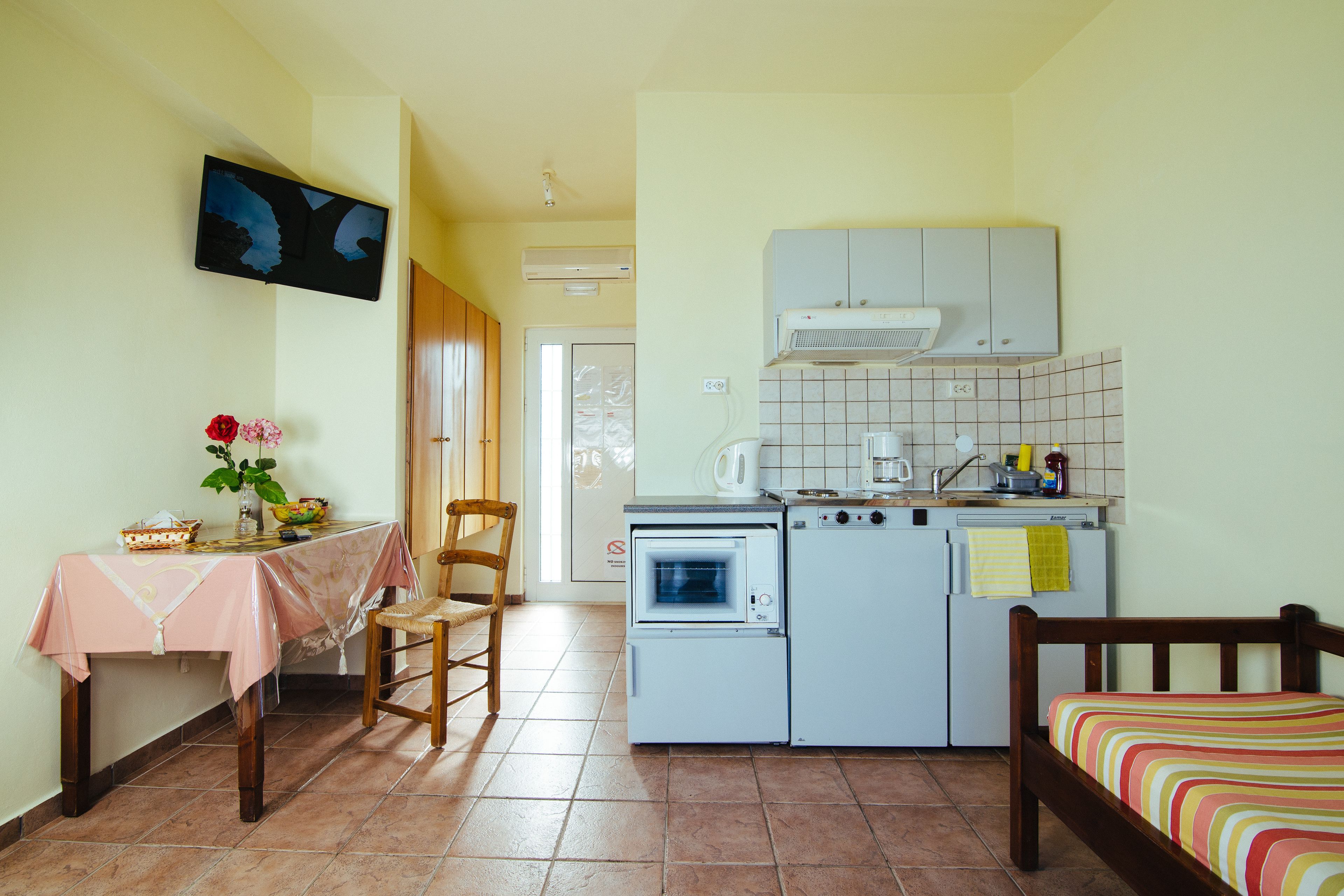 Una cucina compatta con forno a microonde, forno e frigorifero, un tavolo da pranzo con tovaglia rosa e un letto con copripiumino a righe.