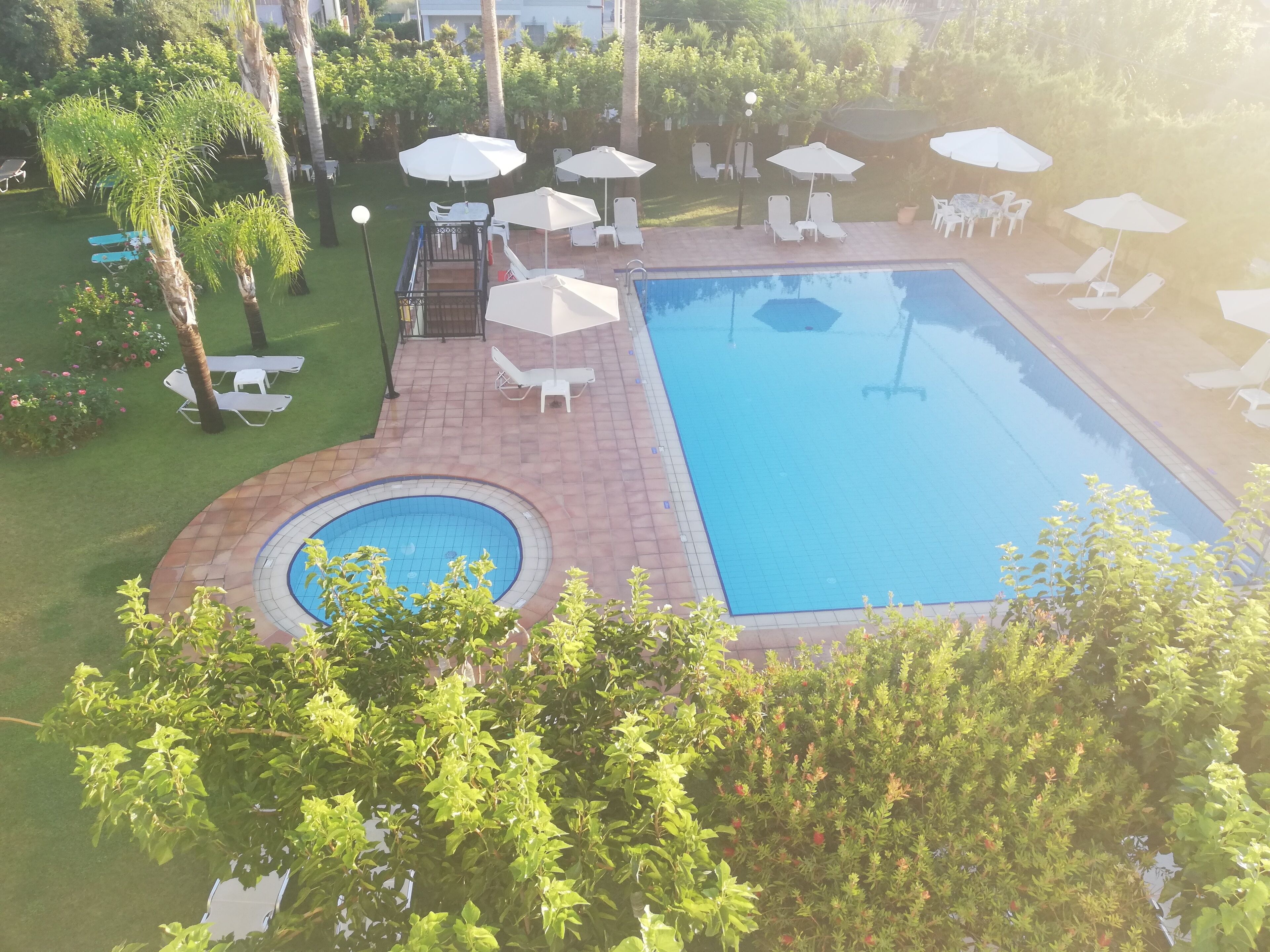 Une piscine dotée de chaises longues et de parasols, entourée de verdure et agrémentée d’une petite terrasse.
