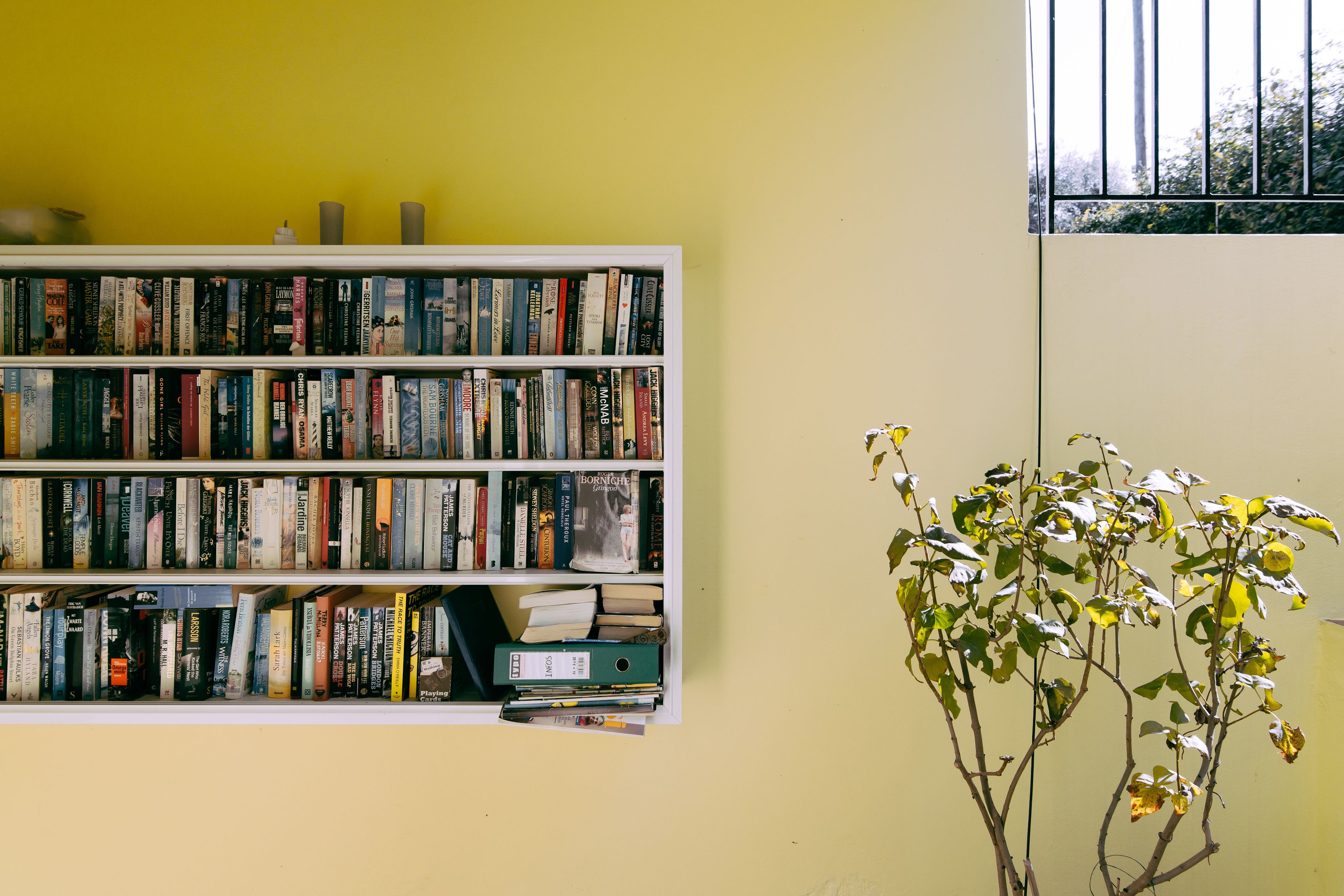 Una estantería llena de libros frente a una pared amarilla.