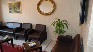 Een woonkamer met een bruine leren bank, twee fauteuils, een bijzettafeltje, een potplant, een ingelijste schilderij en een ronde spiegel aan de muur.