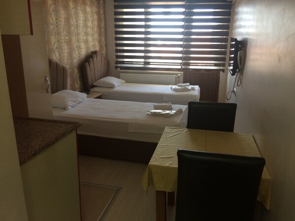 A small, clean room with two single beds, a table, and a chair.