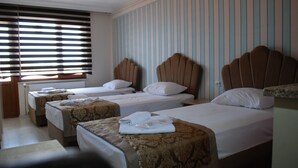 A hotel room with three single beds, each with a headboard, a window with blinds, and a small table with a lamp. - Selimiye  (Edirne)