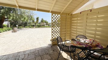 Un espace extérieur abrité, avec une table et des chaises, un tonneau en bois et une cloison en treillis.