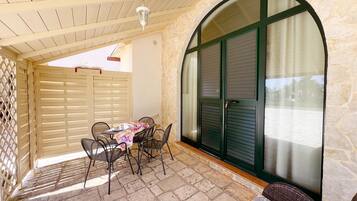 A covered patio with a table and chairs, stone flooring, and a view through a large arched window.