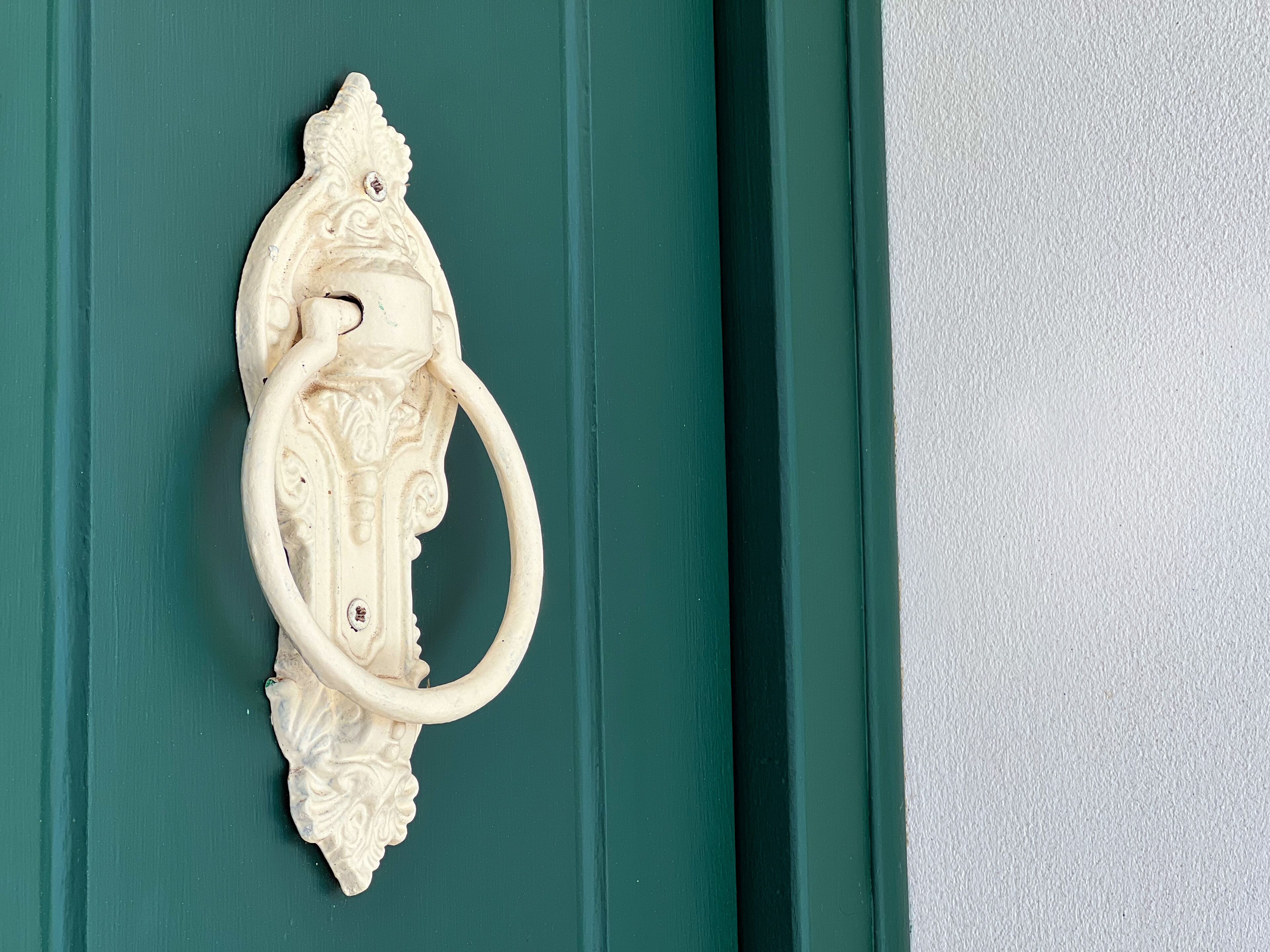 Un llamador blanco y ornamentado, con un pomo circular, sobre una puerta verde.
