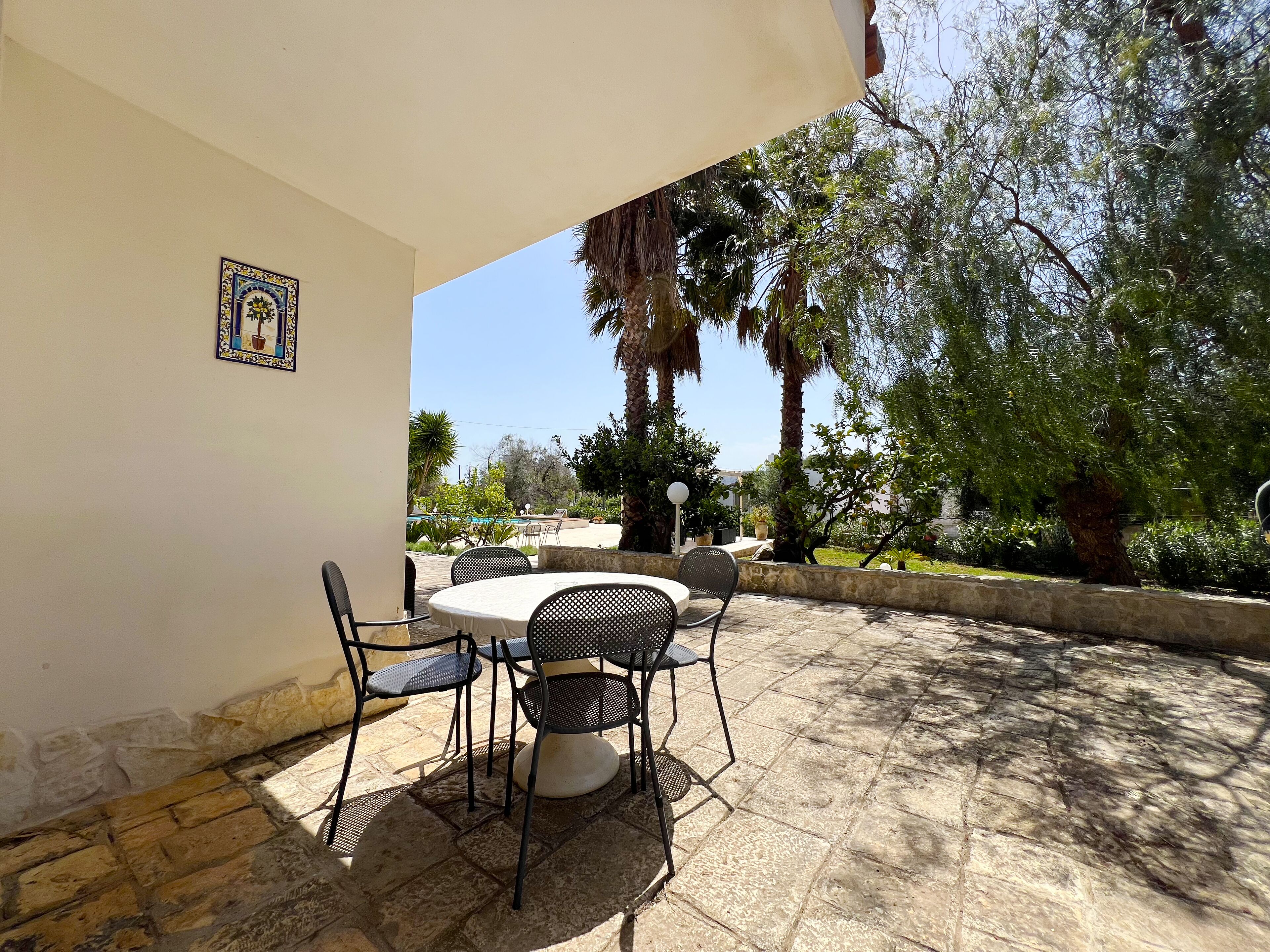 Un patio exterior con una mesa redonda y cuatro sillas, rodeado de suelo de piedra y follaje.