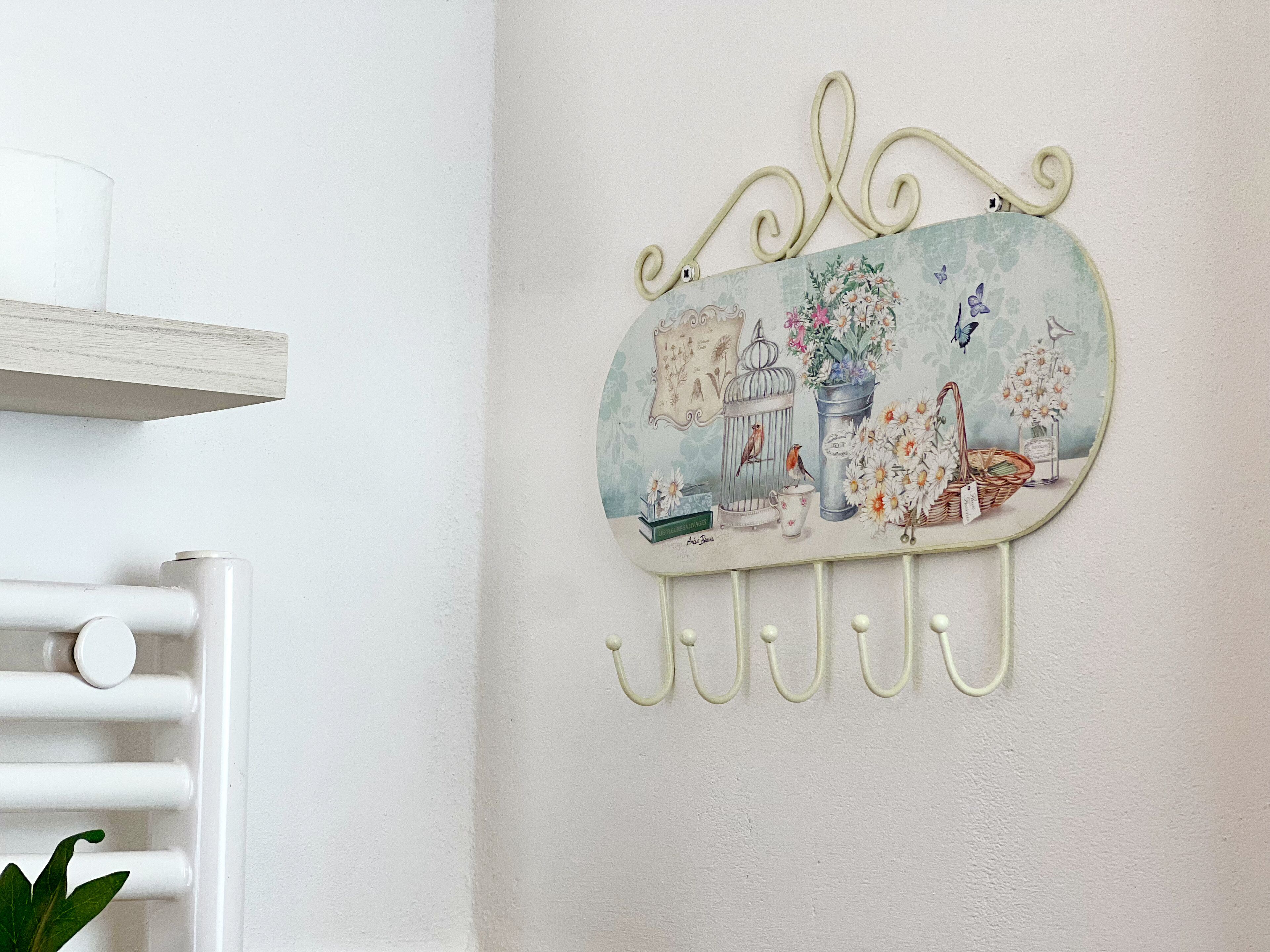 Een decoratief object aan de muur met een vogelkooi, bloemen en een mand.